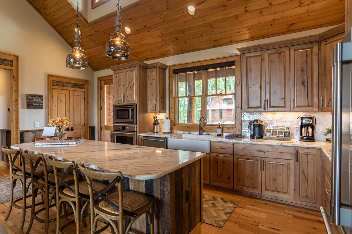 A beautifully appointed kitchen featuring wooden cabinetry, a large kitchen island ideal for casual meals or group prep, and natural light streaming in from adjacent windows. Hanging pendant lights add a touch of modern style while providing a welcoming space for cooking or conversation.