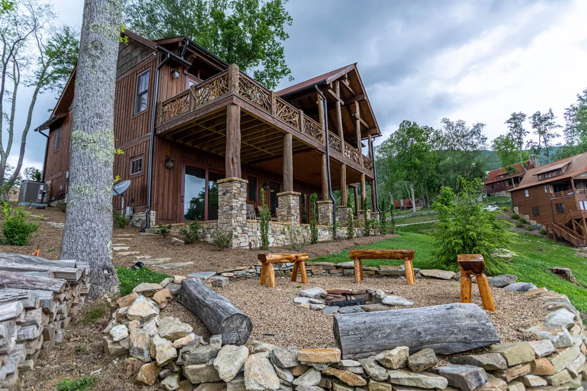 An exterior shot of a wooden deck with a classic fire pit surrounded by stone columns and lush trees. The area is set up for group gatherings, star-gazing, and casual conversations around the fire, blending seamlessly with the natural surroundings.