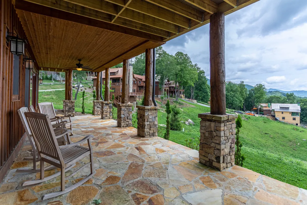 A tranquil porch area with classic rocking chairs, sturdy stone pillars, and a lush green landscape. The scene invites guests to relax outdoors, enjoy the fresh air, and take in the calming mountain surroundings—ideal for unwinding between group activities.