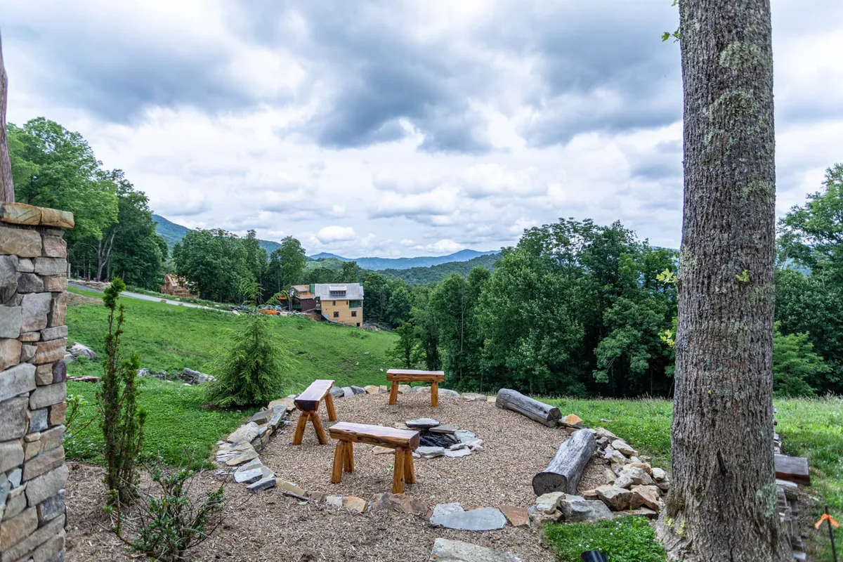 An inviting outdoor fire pit set in a natural landscape, surrounded by wooden benches perfect for group gatherings. The setting offers open sky views, ideal for stargazing or sharing stories under the stars, with sunset light illuminating the mountains in the background.