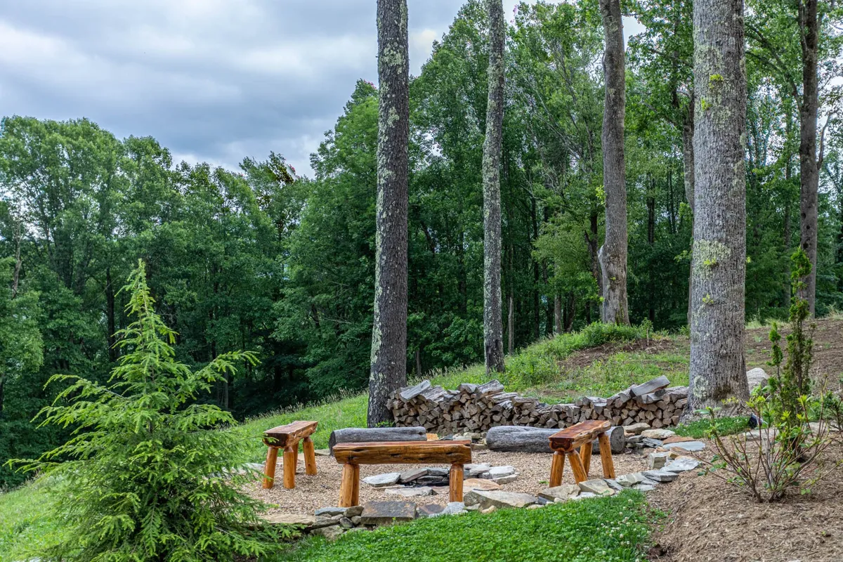 An inviting fire pit area surrounded by wooden benches and trees, creating the perfect outdoor gathering space for storytelling, roasting s'mores, or simply relaxing under the stars.