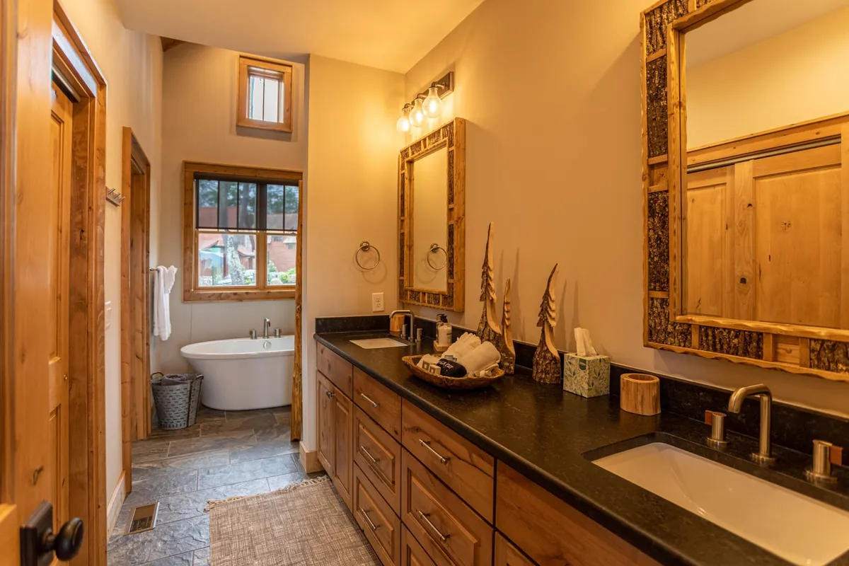 A spa-like ensuite bathroom with a freestanding soaking tub, double vanity with mirrors, and a large window streaming morning light. The mood is calming and indulgent, ideal for unwinding or starting the day refreshed.